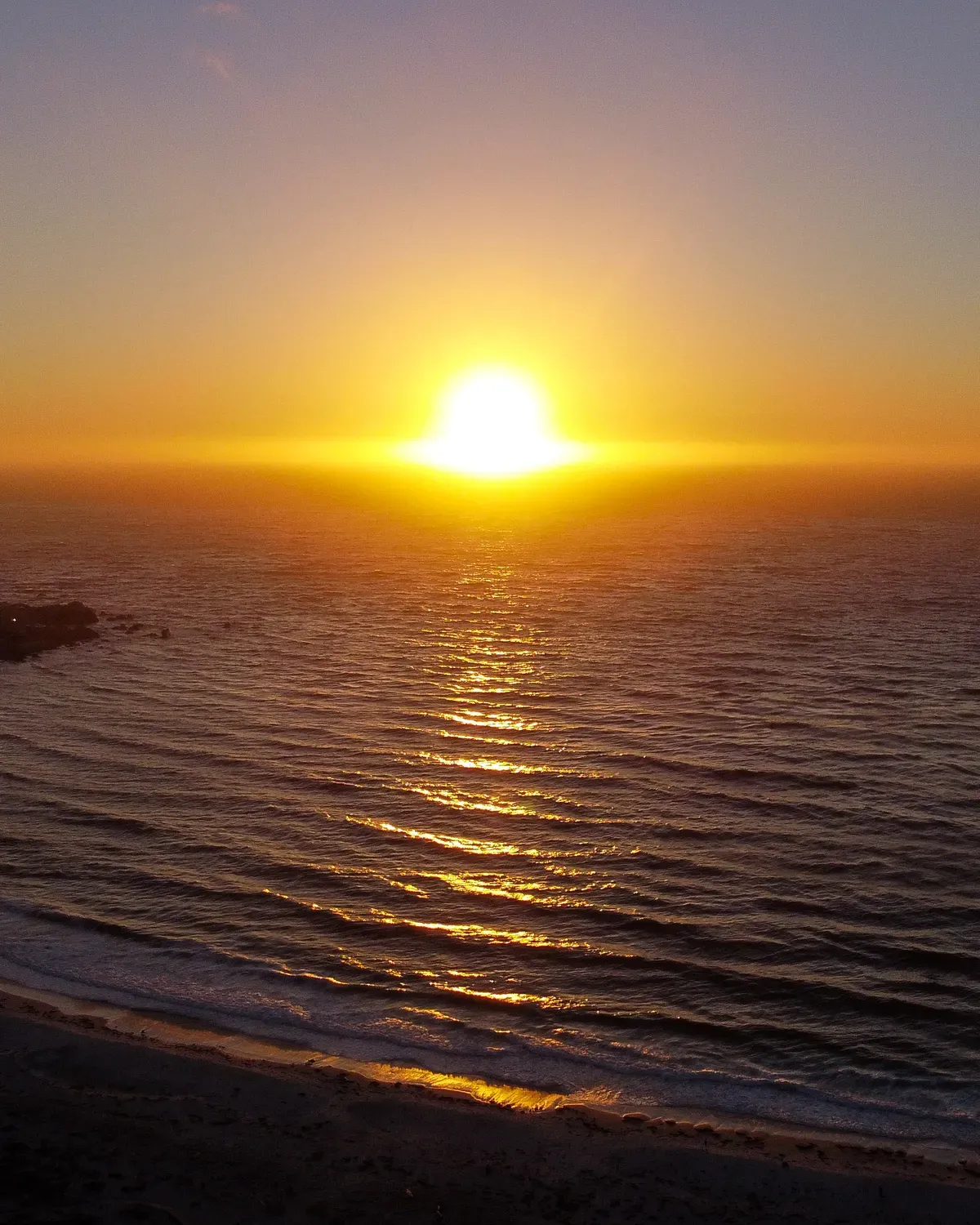 Le soleil posé sur l'horizon au-dessus de l'océan, sa lumière étalée à plat sur l'eau